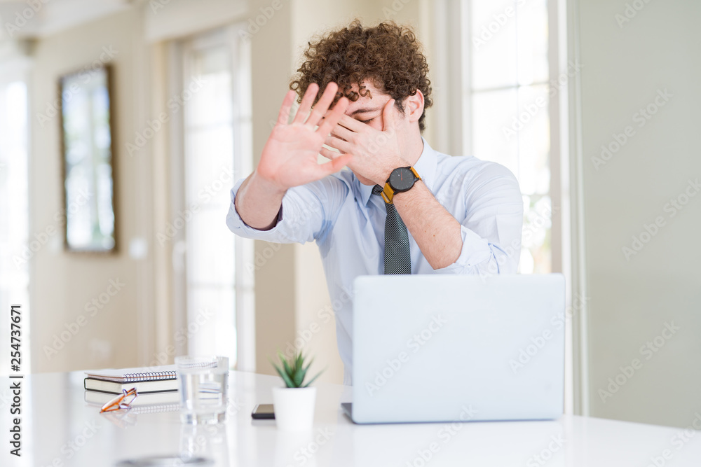 Young business man working with computer laptop at the office covering eyes with hands and doing stop gesture with sad and fear expression. Embarrassed and negative concept.