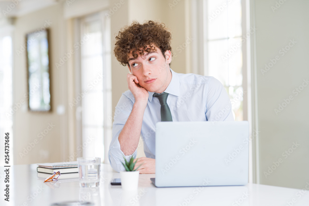 Young business man working with computer laptop at the office thinking looking tired and bored with depression problems with crossed arms.