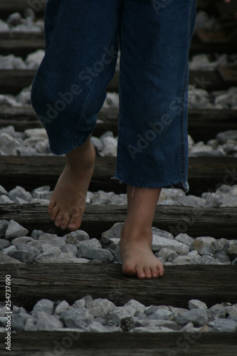 Young boy walks barefoot on abandoned railroad tracks
