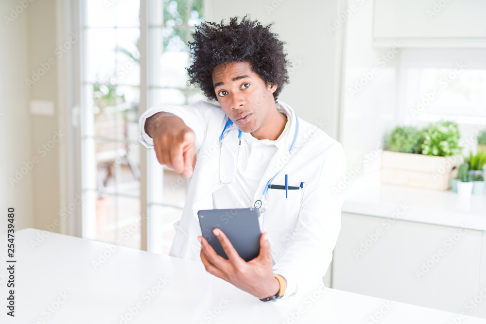 African American doctor man using tablet at the clinic pointing with finger to the camera and to you, hand sign, positive and confident gesture from the front African American doctor man using tablet at the clinic pointing with finger to the camera and to you, hand sign, positive and confident gesture from the front