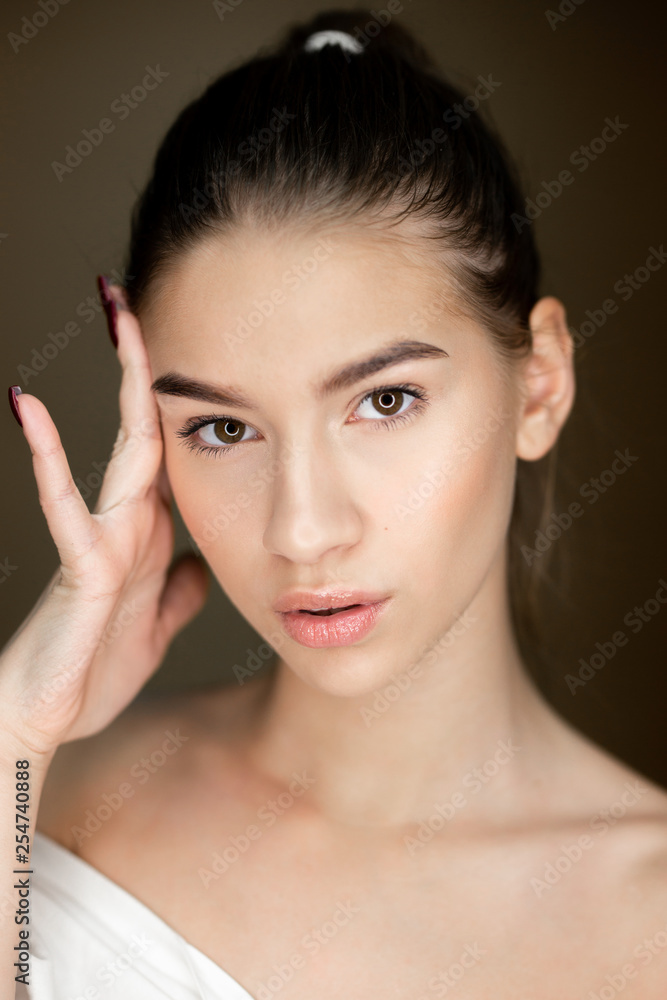 Portrait of young beautiful girl with natural makeup holding her hand on her head
