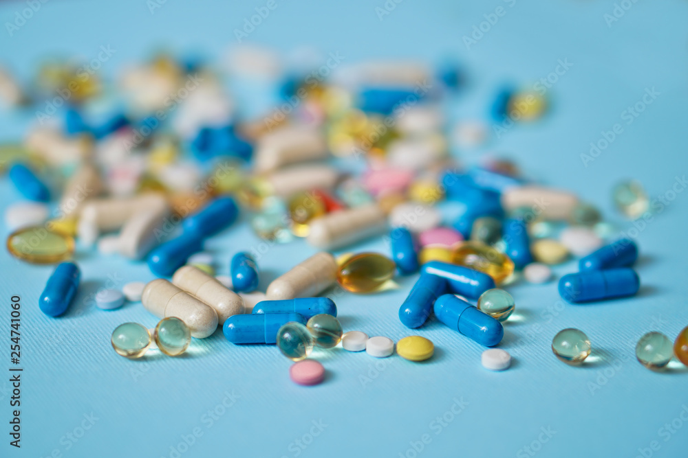 Spilled colored medications and pills on a blue background. Pharmacology and medicine struggle for health. Drug addiction. Treatment of various diseases Spilled colored medications and pills on a blue background. Pharmacology and medicine struggle for health. Drug addiction. Treatment of various diseases