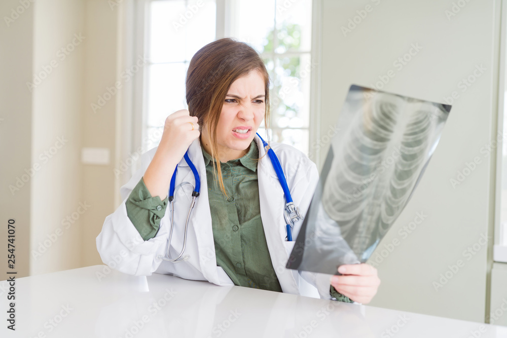 Beautiful young doctor woman looking at chest radiography annoyed and frustrated shouting with anger, crazy and yelling with raised hand, anger concept Beautiful young doctor woman looking at chest radiography annoyed and frustrated shouting with anger, crazy and yelling with raised hand, anger concept