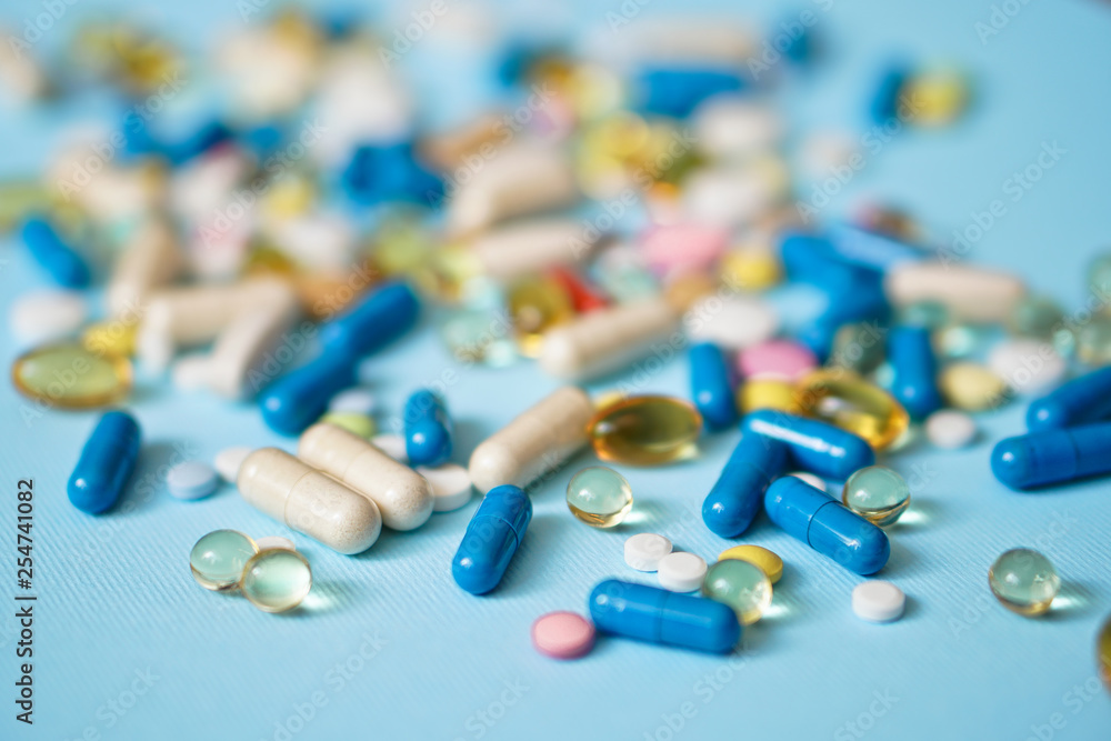 Spilled colored medications and pills on a blue background. Pharmacology and medicine struggle for health. Drug addiction. Treatment of various diseases Spilled colored medications and pills on a blue background. Pharmacology and medicine struggle for health. Drug addiction. Treatment of various diseases