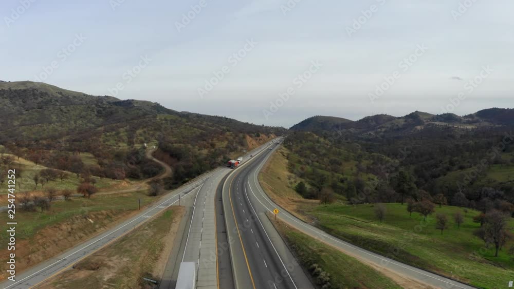 Semi trucks driving on highway through green mountains, AERIAL VIEW Semi trucks driving on highway through green mountains, AERIAL VIEW
