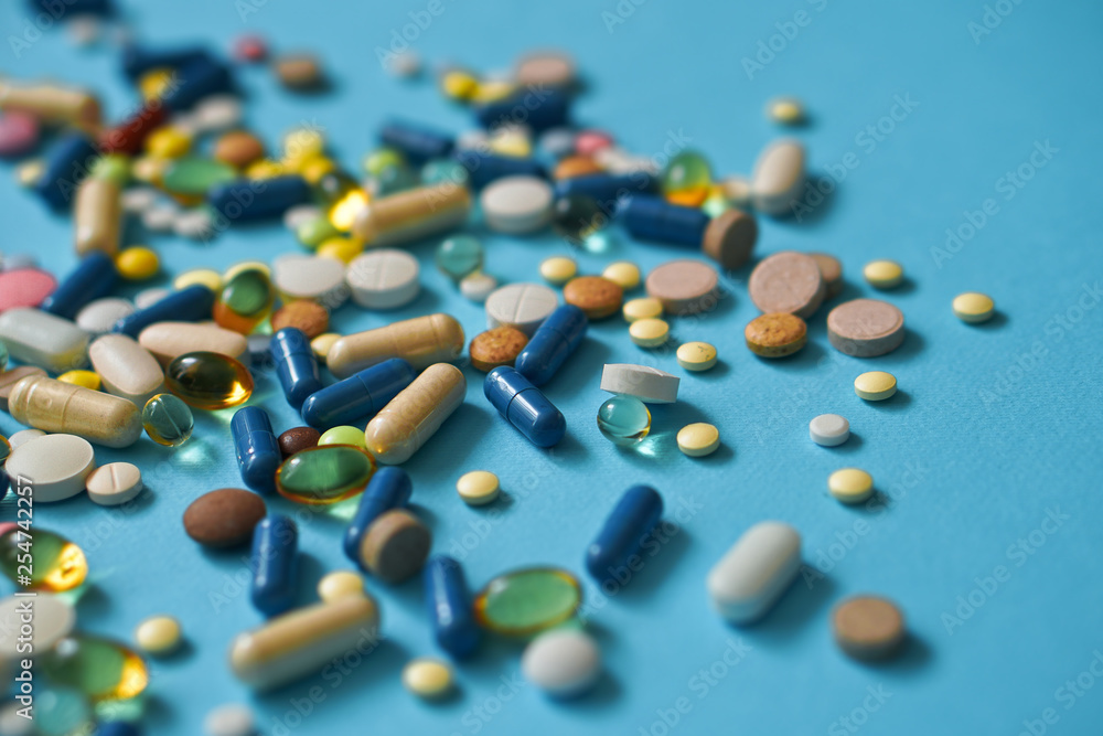 Spilled colored medications and pills on a blue background. Pharmacology and medicine struggle for health. Drug addiction. Treatment of various diseases Spilled colored medications and pills on a blue background. Pharmacology and medicine struggle for health. Drug addiction. Treatment of various diseases