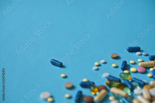 Spilled colored medications and pills on a blue background. Pharmacology and medicine struggle for health. Drug addiction. Treatment of various diseases