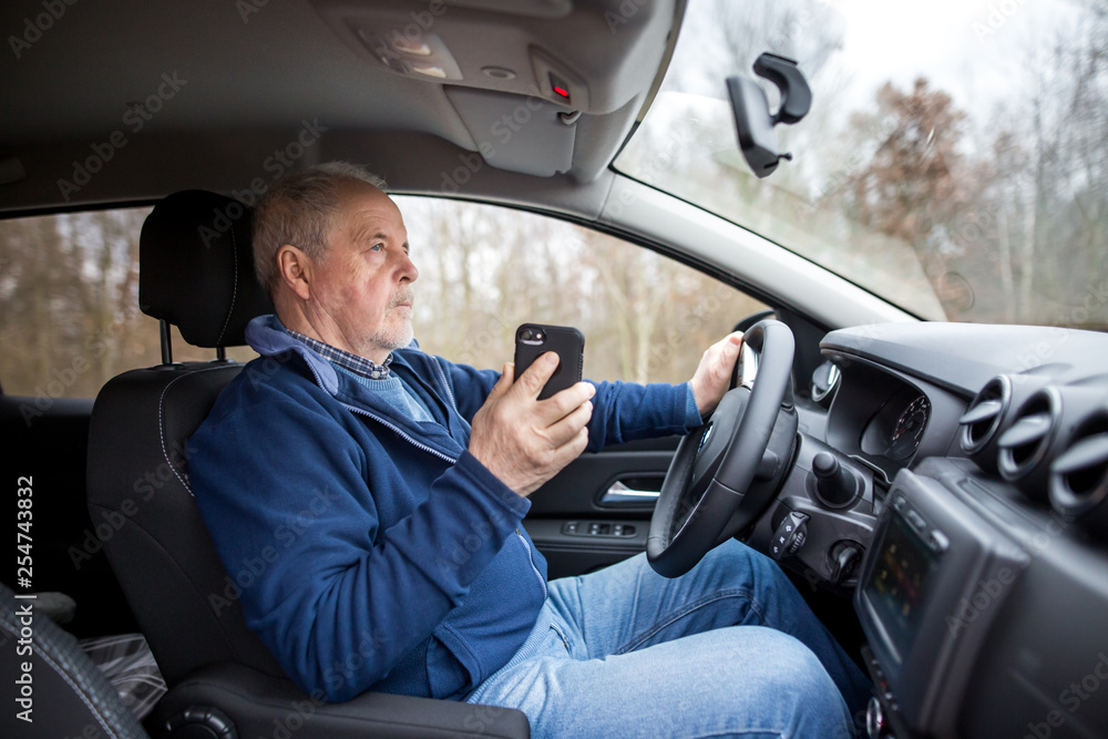 Senior man using a smartphone while riding his new, modern car, transportation concept