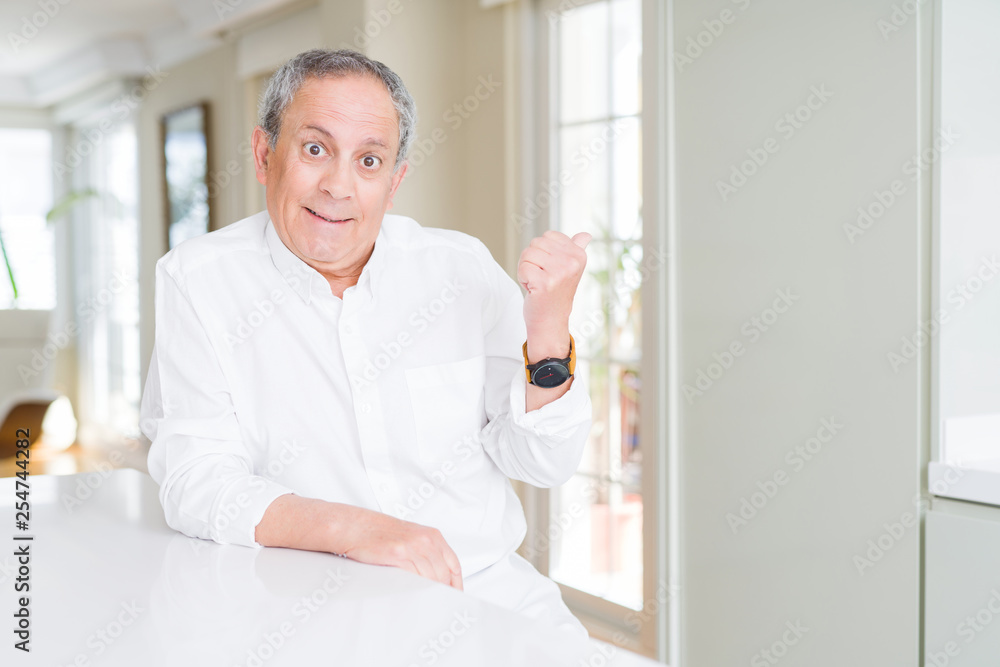 Handsome senior man at home smiling with happy face looking and pointing to the side with thumb up.