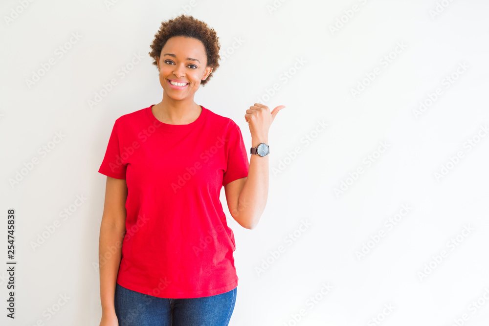 Young beautiful african american woman over white background smiling with happy face looking and pointing to the side with thumb up.