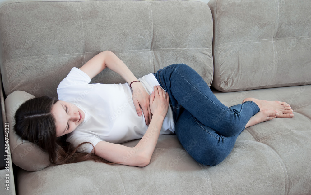 The girl has a stomachache. A woman lies on the couch, is sick, she has a stomach ache. Abdominal pain.