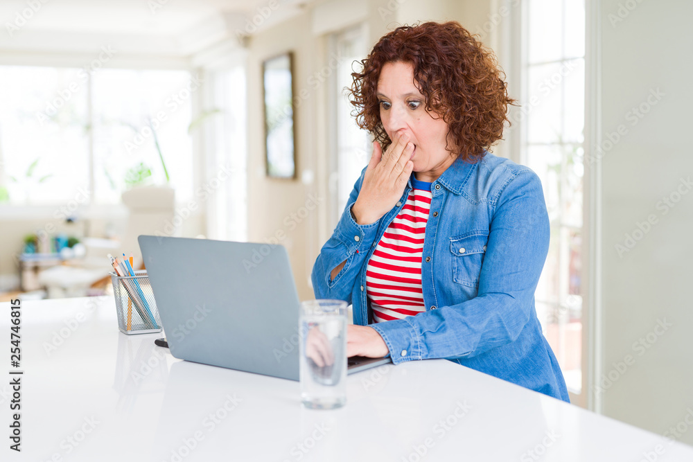 Obraz premium Senior woman working using computer laptop cover mouth with hand shocked with shame for mistake, expression of fear, scared in silence, secret concept