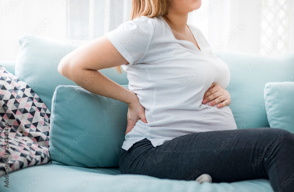 Pregnant woman suffering from backache on sofa at home Pregnant woman suffering from backache on sofa at home