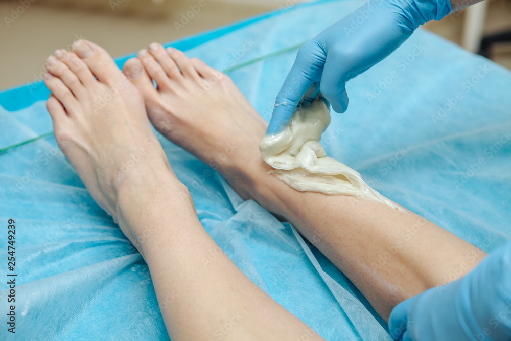 Fototapeta premium Epilation wax in the spa salon. Beautician imposes wax on women's legs. Close-up.