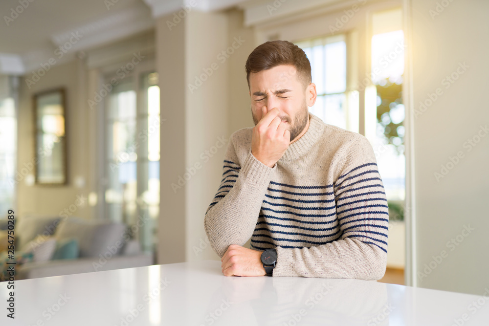 Young handsome man at home smelling something stinky and disgusting, intolerable smell, holding breath with fingers on nose. Bad smells concept. Young handsome man at home smelling something stinky and disgusting, intolerable smell, holding breath with fingers on nose. Bad smells concept.