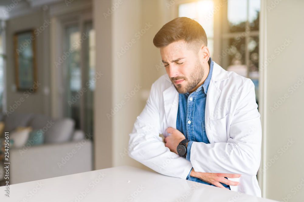 Young handsome doctor man at the clinic with hand on stomach because nausea, painful disease feeling unwell. Ache concept.