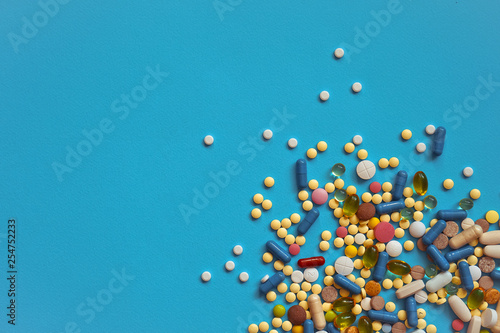Spilled colored medications and pills on a blue background. Pharmacology and medicine struggle for health. Drug addiction. Treatment of various diseases photo