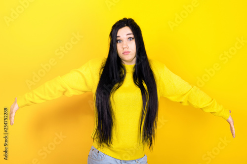 Surprised terrified female gestures with uncertainty, stares at camera, puzzled as doesn`t know anwser on tricky question, emotional girl in a yellow sweater, image on a yellow background photo