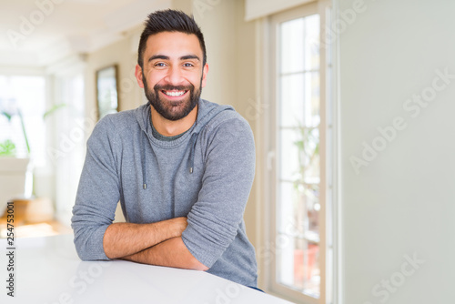 Handsome hispanic man wearing casual sweatshirt at home happy face smiling with crossed arms looking at the camera. Positive person.