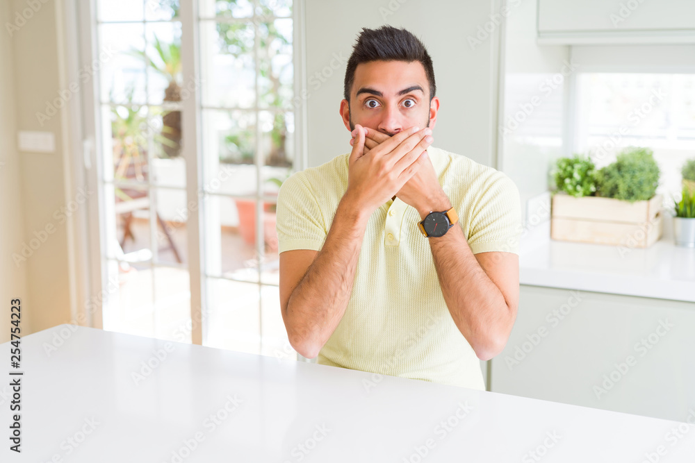 Handsome hispanic man casual yellow t-shirt at home shocked covering mouth with hands for mistake. Secret concept. Handsome hispanic man casual yellow t-shirt at home shocked covering mouth with hands for mistake. Secret concept.