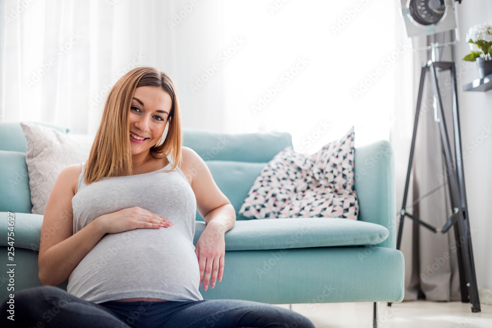 Beautiful smiling pregnant woman sitting on floor at home, looking at camera Beautiful smiling pregnant woman sitting on floor at home, looking at camera