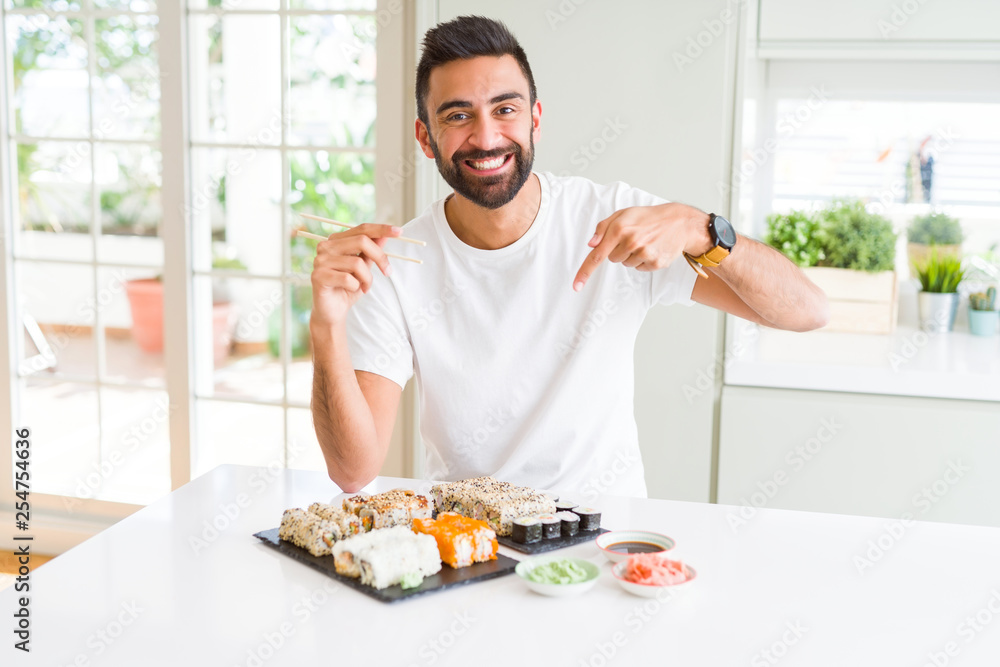 Handsome hispanic man eating asian sushi using chopsticks very happy pointing with hand and finger Handsome hispanic man eating asian sushi using chopsticks very happy pointing with hand and finger