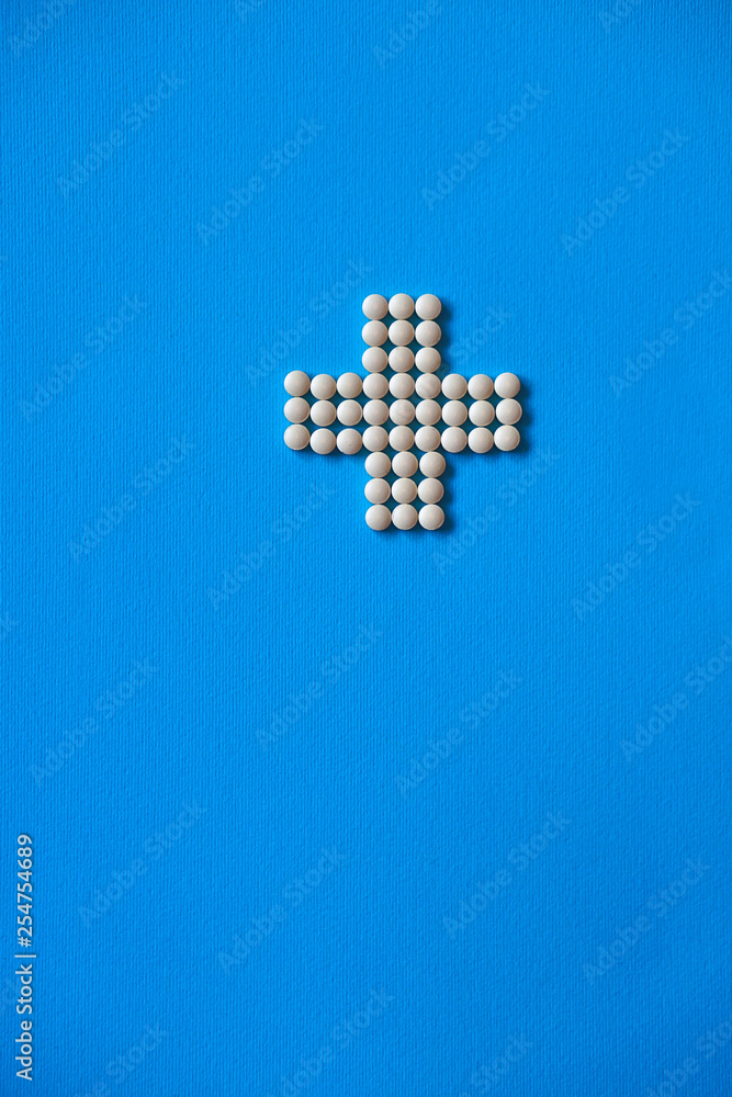 Obraz premium Medical cross laid out medicines, white tablets on a blue background. Pharmacology and medicine struggle for health. Drug addiction. Treatment of various diseases