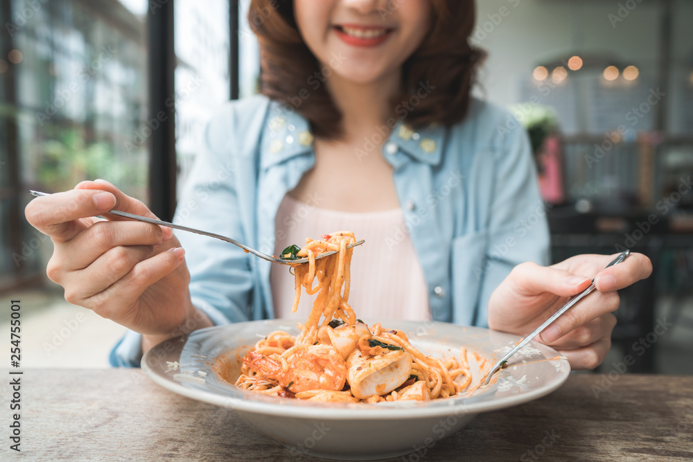 Beautiful happy Asian woman eating a plate of Italian seafood spaghetti at restaurant or cafe while smiling and looking at food. Beautiful happy Asian woman eating a plate of Italian seafood spaghetti at restaurant or cafe while smiling and looking at food.