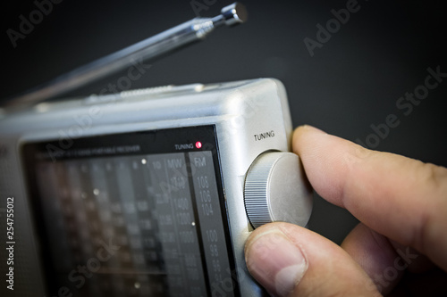 Portable radio (FM and shortwave); man's hand on tuning dial.