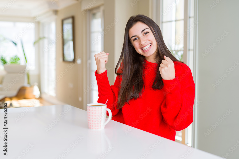 Beautiful young woman drinking a cup of black coffee celebrating surprised and amazed for success with arms raised and open eyes. Winner concept.