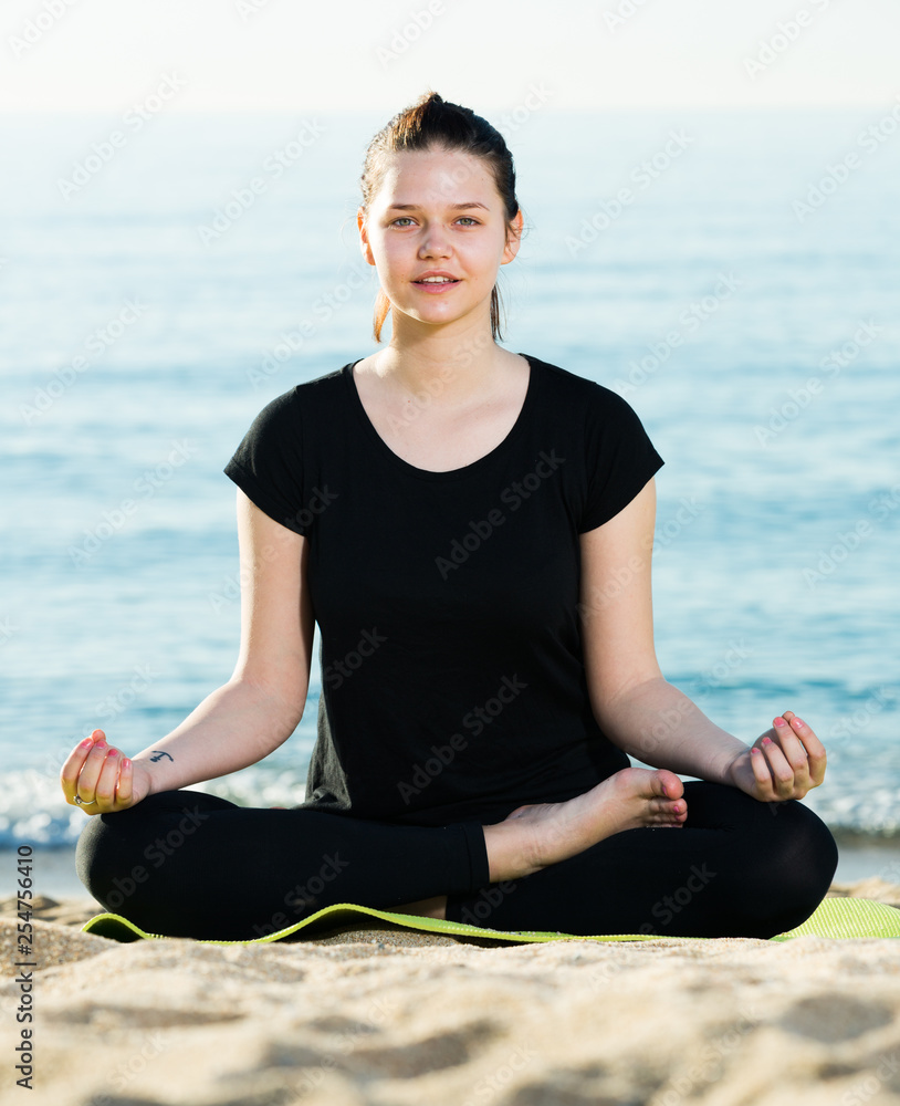 Fototapeta premium Girl in black T-shirt is sitting and doing meditation