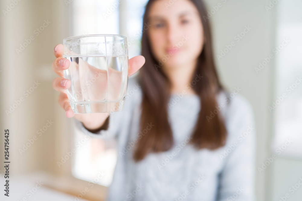 Beautiful young woman drinking a fresh glass of water with a confident expression on smart face thinking serious Beautiful young woman drinking a fresh glass of water with a confident expression on smart face thinking serious