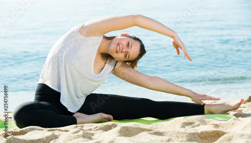 Smiling adult female in white T-shirt is practicing set of stretching exercises