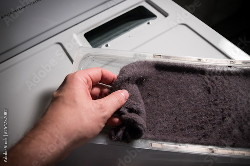 Hand cleaning accumulated clothing lint from trap in clothes dryer.