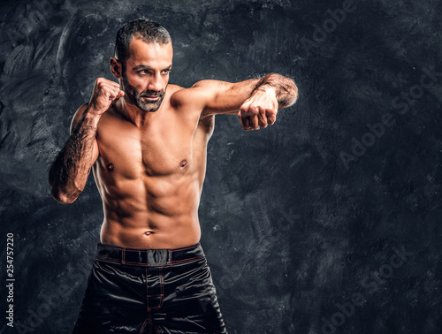 Professional fighter showing kick fighting technique. Studio photo against a dark textured wall
