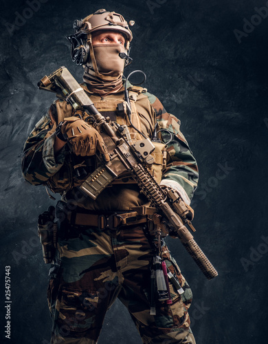 Special forces soldier in military uniform posing with assault rifle. Studio photo against a dark textured wall