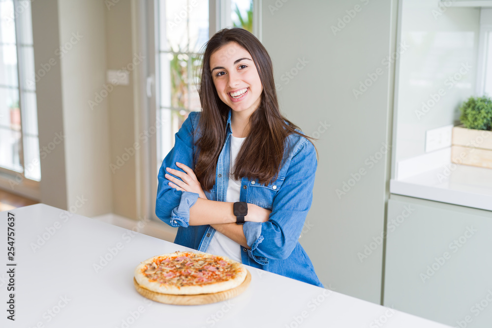 Beautiful young woman eating homemade tasty pizza at the kitchen happy face smiling with crossed arms looking at the camera. Positive person. Beautiful young woman eating homemade tasty pizza at the kitchen happy face smiling with crossed arms looking at the camera. Positive person.