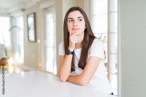 Beautiful young woman wearing casual white t-shirt with hand on chin thinking about question, pensive expression. Smiling with thoughtful face. Doubt concept.