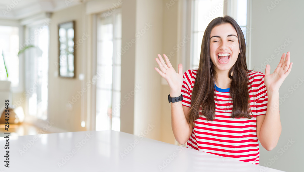Beautiful young woman wearing casual stripes t-shirt celebrating mad and crazy for success with arms raised and closed eyes screaming excited. Winner concept Beautiful young woman wearing casual stripes t-shirt celebrating mad and crazy for success with arms raised and closed eyes screaming excited. Winner concept