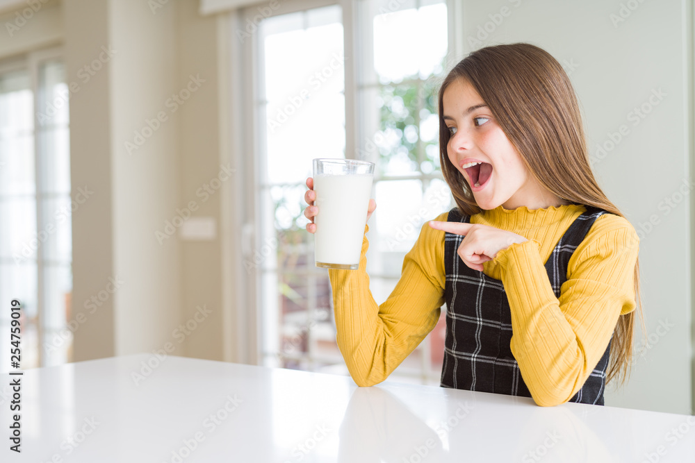 Beautiful young girl driking a glass of fresh milk very happy pointing with hand and finger Beautiful young girl driking a glass of fresh milk very happy pointing with hand and finger
