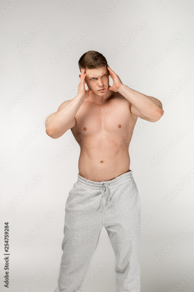 Portrait of young shirtless unhappy bodybuilder holding hands near head