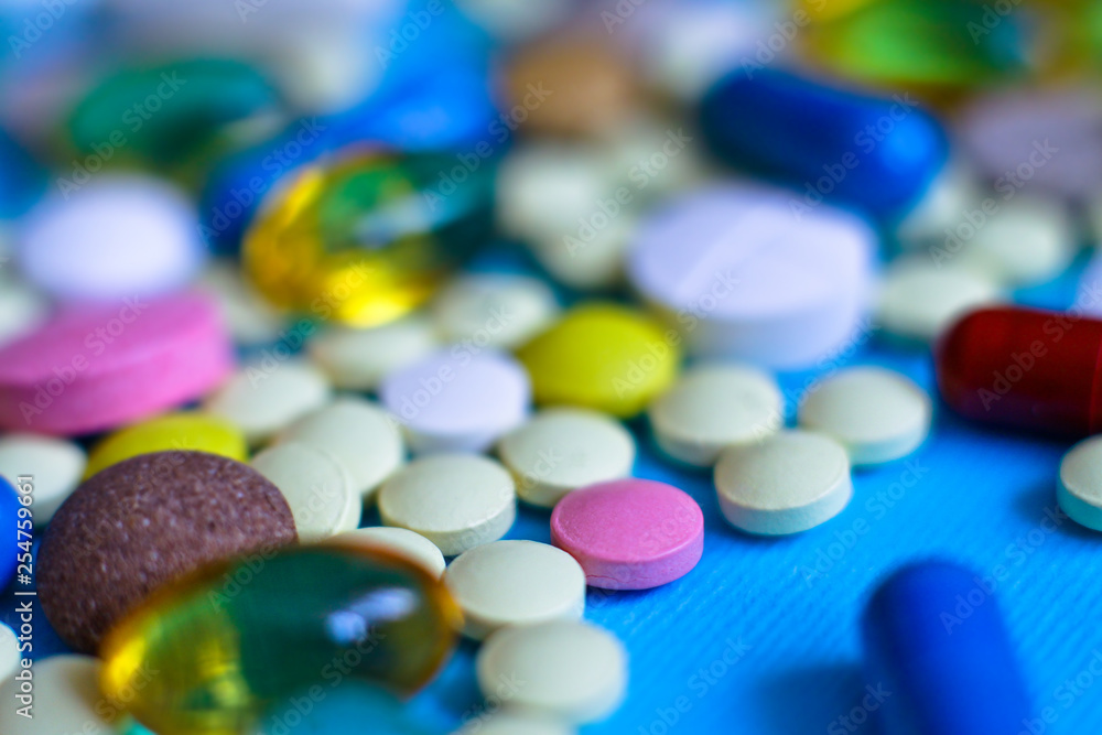 Spilled colored medications and pills on a blue background. Pharmacology and medicine struggle for health. Drug addiction. Treatment of various diseases Spilled colored medications and pills on a blue background. Pharmacology and medicine struggle for health. Drug addiction. Treatment of various diseases