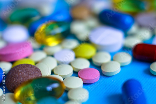 Spilled colored medications and pills on a blue background. Pharmacology and medicine struggle for health. Drug addiction. Treatment of various diseases