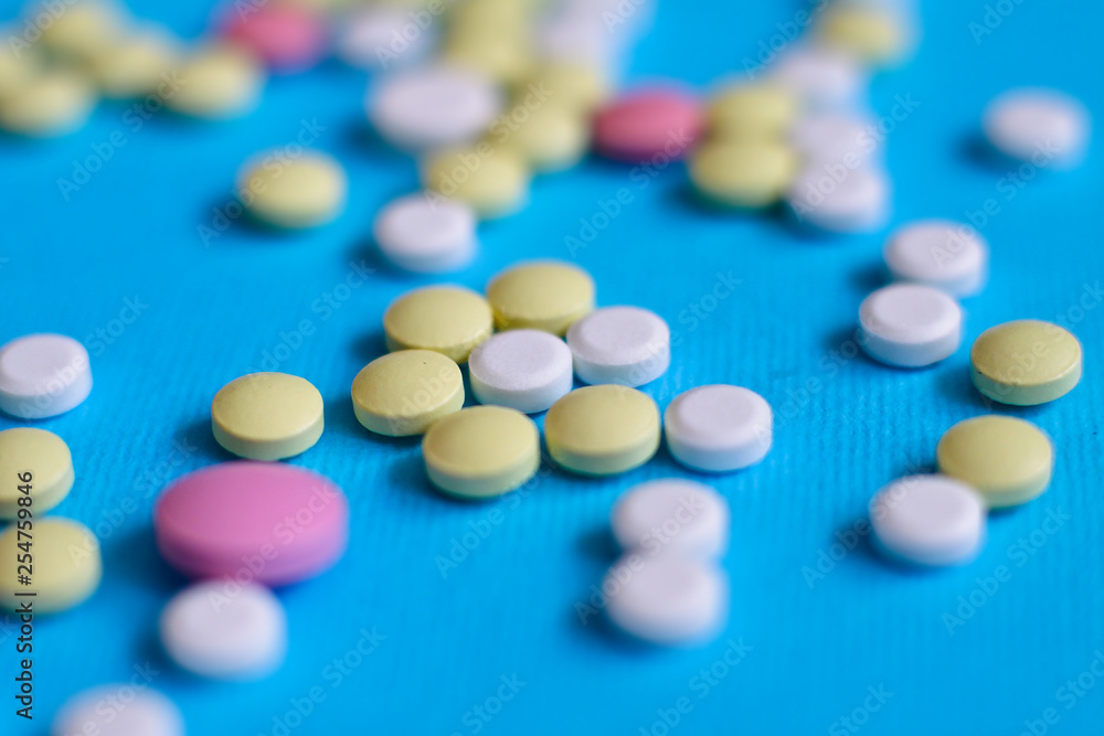 Spilled colored medications and pills on a blue background. Pharmacology and medicine struggle for health. Drug addiction. Treatment of various diseases Spilled colored medications and pills on a blue background. Pharmacology and medicine struggle for health. Drug addiction. Treatment of various diseases