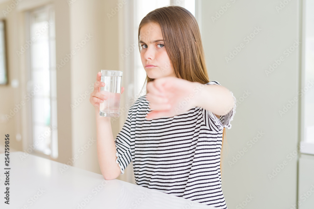 Beautiful young girl kid drinking a fresh glass of water with angry face, negative sign showing dislike with thumbs down, rejection concept Beautiful young girl kid drinking a fresh glass of water with angry face, negative sign showing dislike with thumbs down, rejection concept