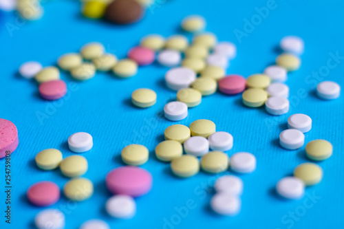 Spilled colored medications and pills on a blue background. Pharmacology and medicine struggle for health. Drug addiction. Treatment of various diseases