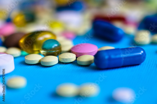 Spilled colored medications and pills on a blue background. Pharmacology and medicine struggle for health. Drug addiction. Treatment of various diseases