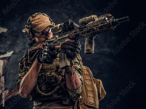 Private security service contractors, the elite special unit, full protective soldier holding assault rifle aiming at the target. Studio photo against a dark wall. 