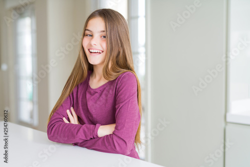 Beautiful young girl kid on white table happy face smiling with crossed arms looking at the camera. Positive person.