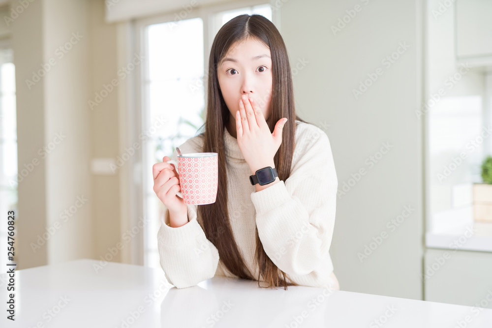 Beautiful Asian woman drinking a cup of coffee cover mouth with hand shocked with shame for mistake, expression of fear, scared in silence, secret concept Beautiful Asian woman drinking a cup of coffee cover mouth with hand shocked with shame for mistake, expression of fear, scared in silence, secret concept